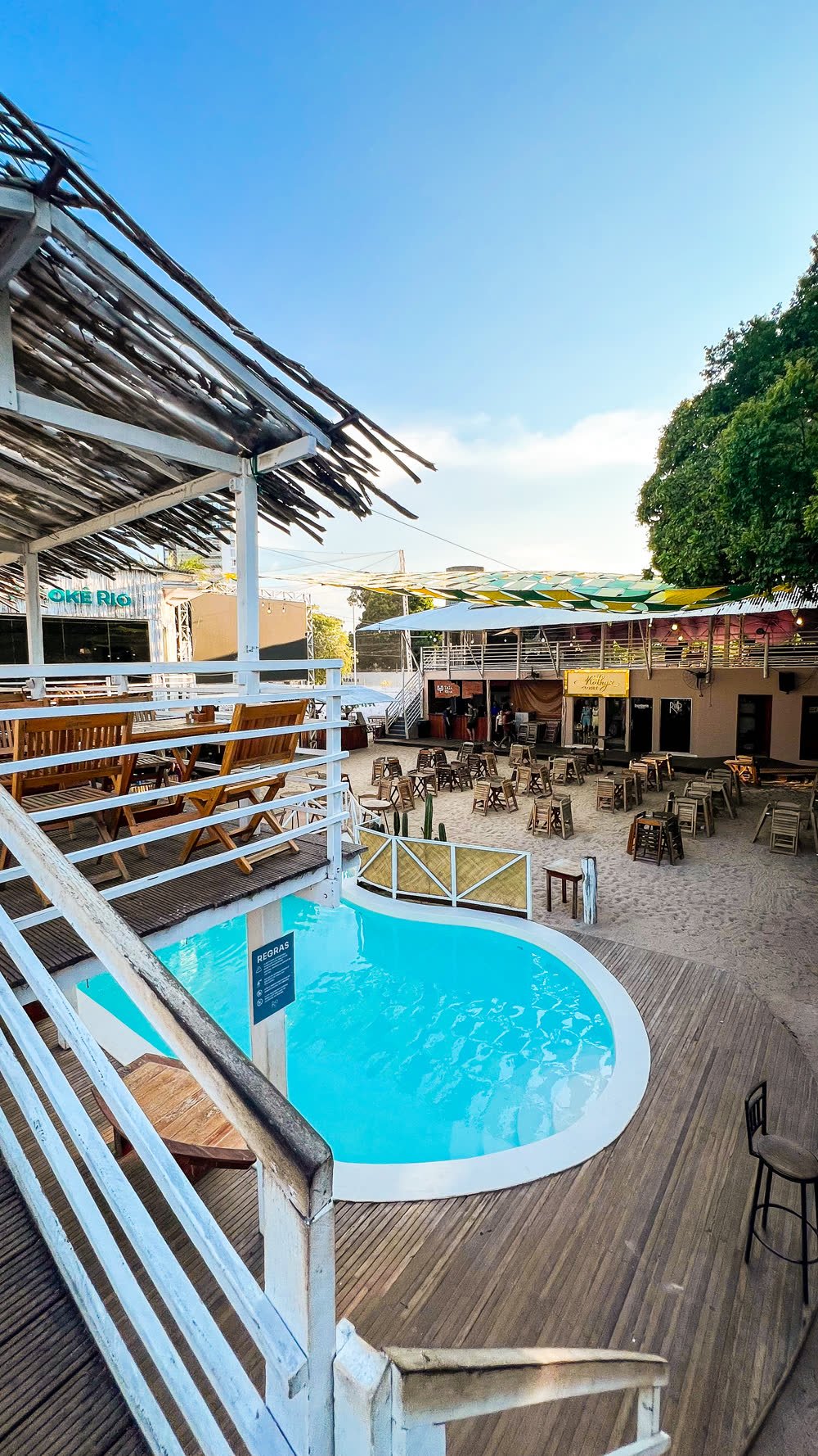 Piscina com deck de madeira do Rio Sand Club, com mesas na areia ao fundo