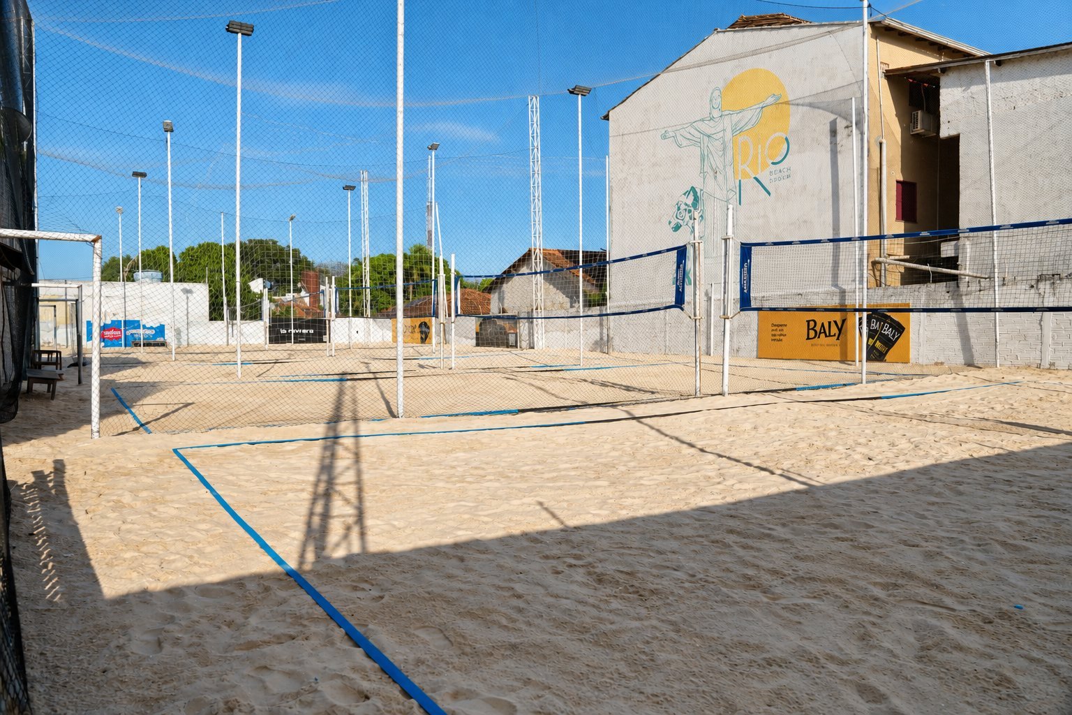 Quadras de areia do Rio Sand Club com redes de vôlei montadas e o mural do Rio ao fundo